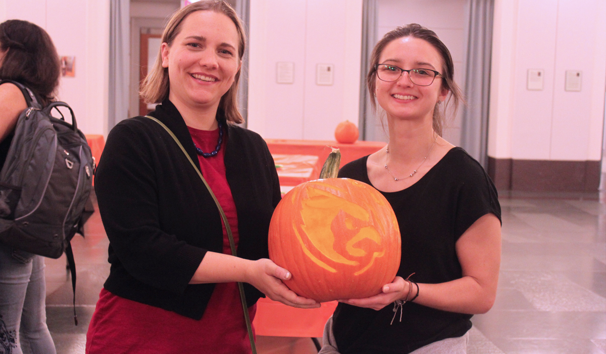 two students holding a carved pumpkin