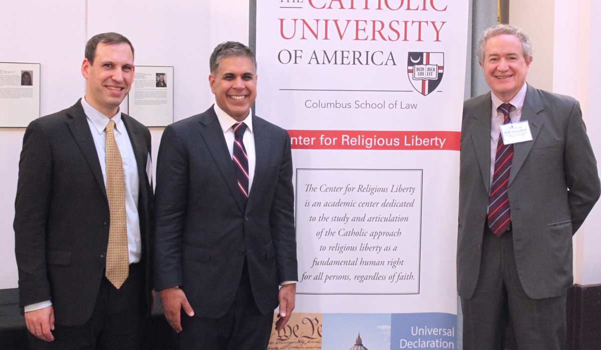 3 speakers posing with banner