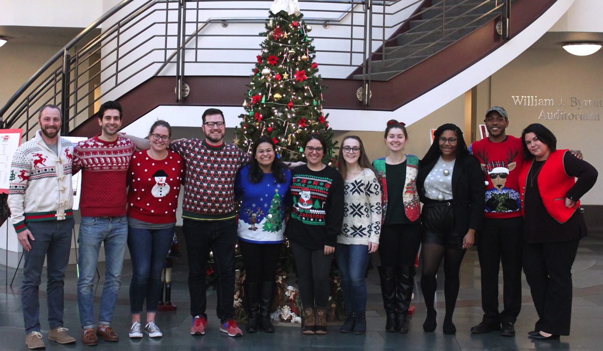 Law students and staff pose in Christmas sweaters in front of the law school's Christmas tree in the atrium