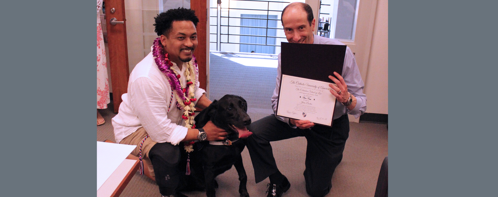 A law student having his service dog presented with a diploma from the registrar