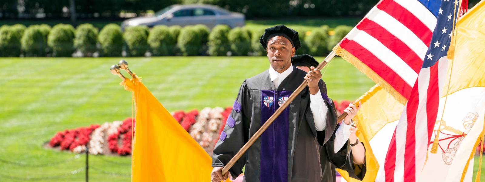 A Student walking into Commencement holding the US Flag
